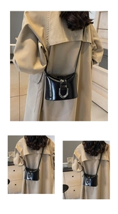 Detail of glossy black bucket bag featuring a silver horseshoe buckle and slim strap