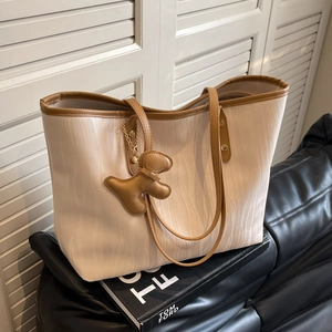 Cream tote bag with brown trim, wave texture, and bear charm on a leather sofa