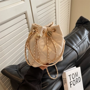 Secchiello in pelle trapuntata beige con catena dorata su uno sfondo moderno