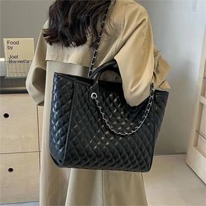 Classic black quilted leather tote bag with chain strap shown on model in street style