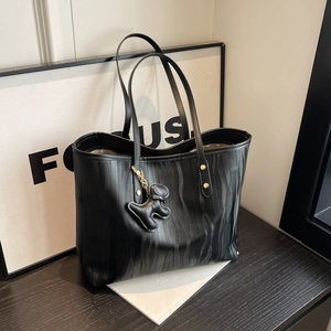 Black tote bag with zebra ripple texture and dog charm displayed on a black wooden table