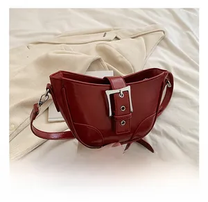 Détail du sac demi-lune rouge brillant avec grande boucle argentée sur tissu blanc