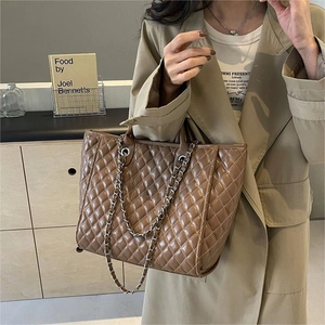 Deep brown quilted tote bag with silver chain straps worn with a stylish beige trench coat