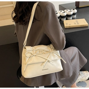 Detail of cream white shoulder bag featuring delicate bow ornaments and ruched flap design