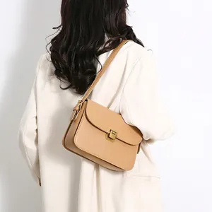 Camel leather crossbody square bag with gold buckle worn on a white suit jacket