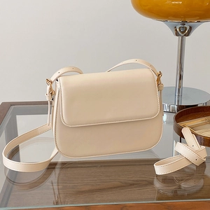 Sac bandoulière minimaliste en cuir crème avec boucle dorée sur surface bois