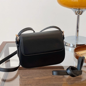 Sac bandoulière minimaliste en cuir noir avec ferrures dorées sur table en bois