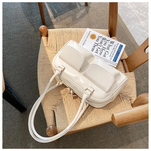 Close-up of cream faux leather handbag featuring double flap pockets on a woven chair
