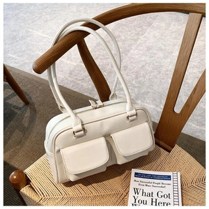 Detail view of cream white shoulder bag with dual front pockets on a wooden chair