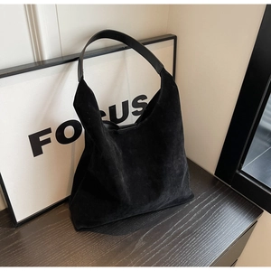 Detail of black suede hobo bag with smooth leather strap and large capacity on wooden surface