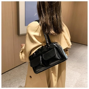 Detail view of a black retro shoulder bag with two front pockets on a beige trench coat