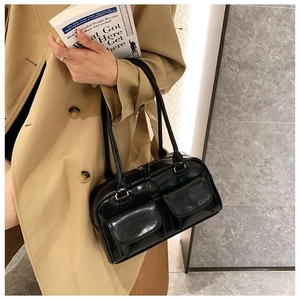 Close-up of black retro shoulder bag with dual front pockets on a model wearing a khaki coat