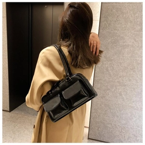 Detail of a black glossy leather underarm bag with double front flap pockets on a model