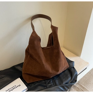 Detail view of large dark brown suede tote bag resting on a textured leather garment