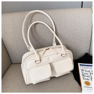 Detail of a creamy white rectangular leather handbag with dual pockets on a grey sofa