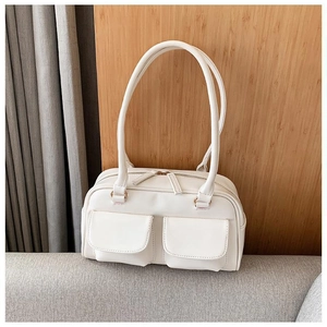 Detailed view of white faux leather handbag with two front pockets on a grey sofa