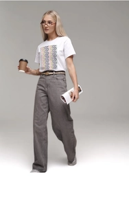 Detail of bohemian diamond pattern on white cotton t-shirt with high-waist grey wide-leg jeans