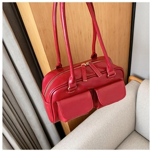 Close-up of red glossy leather shoulder bag featuring dual front pockets and gold zippers