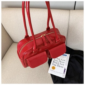 Close-up of red leather handbag with double front pockets and shoulder straps on a sofa