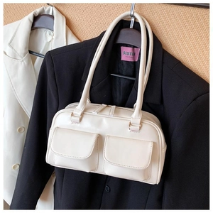 Detail of cream white leather handbag with dual front pockets against a black blazer