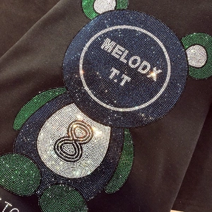Gros plan d'un ours en strass bleus et verts étincelants sur un t-shirt en coton noir