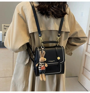 Rear view of model wearing black structured backpack with white bead trim and rabbit charm