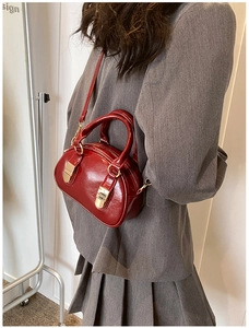 Close-up of a red patent leather bowling bag with gold hardware on a grey blazer suit