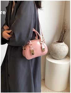 Detail view of pink leather bowling bag with gold buckles on a grey blazer model