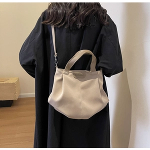 Side view of beige canvas tote bag with dual handles and slim strap worn by a model