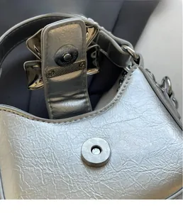 Detail of silver metallic textured bag featuring magnetic closure and bow ornament