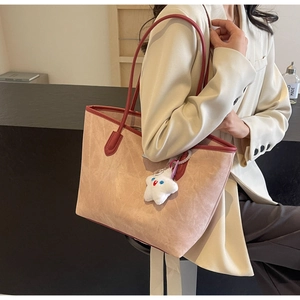 Macro detail of high-capacity beige tote bag with star charm and contrast red handles
