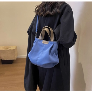 Blue canvas tote bag with brown leather handles worn by model in a minimalist setting
