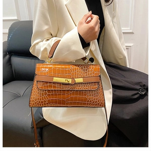 Dettaglio di una borsa marrone in pelle goffrata coccodrillo con fibbia dorata su modella