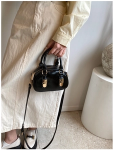 Close-up of elegant black glossy bowling handbag with gold hardware held by a model