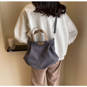 Detail of dark grey canvas tote bag with brown leather handles and brand label