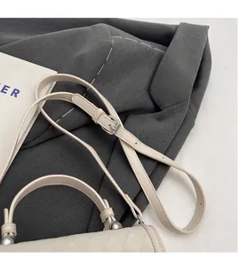 Detail of adjustable slender strap and silver buckle on a quilted beige crossbody bag