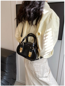 Back view of model carrying a black patent leather bowling bag with gold metal buckles