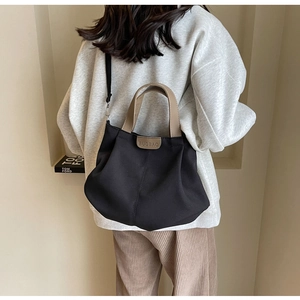 Detailed back view of a black canvas tote bag with khaki leather straps on a model