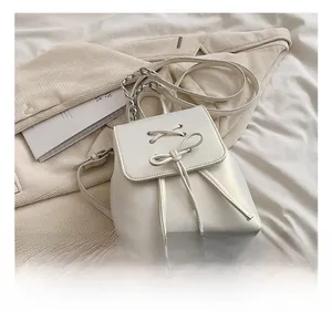 Detail of white leather mini backpack showing the lace-up bow and metal chain strap