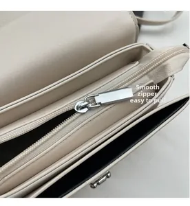 Detail view of smooth silver zipper and stitching on a beige quilted crossbody bag