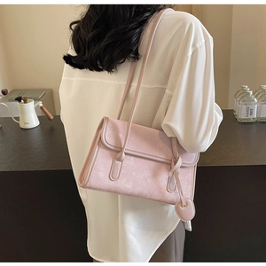 Detail of light pink suede shoulder bag with heart charm shown on a female model