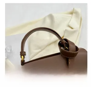 Close-up of brown matte leather handbag handle with knot detail and gold hardware