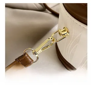 Close-up of golden metal hook on white woven bucket bag with brown leather strap