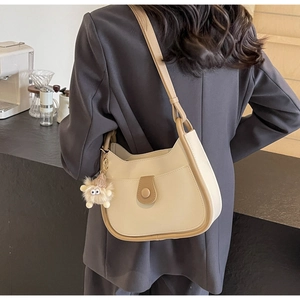Creamy white shoulder bag with brown trim and cute plush charm on model in cafe