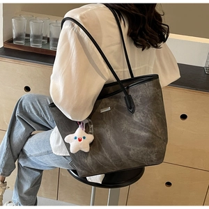 Detail view of a large marble texture tote bag with star plush charm and black leather straps