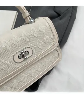 Detail of quilted texture and silver rotary lock on cream-white crossbody bag