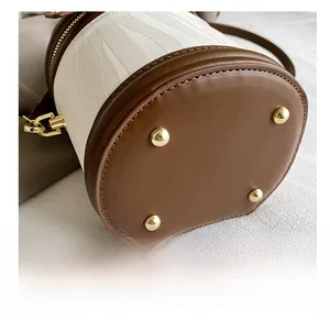 Detail view of the cylinder bucket bag featuring durable brown leather bottom with gold studs