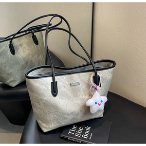 Detail of a large tote bag with textured finish, slim black handles, and a star plush charm