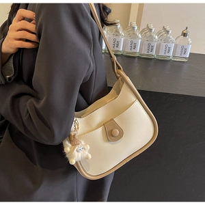 Detail of cream and brown shoulder bag with a cute plush monster charm and fine stitching