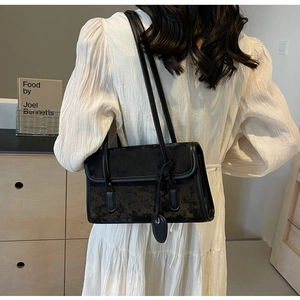 Close-up of black retro shoulder bag with textured fabric on a model in a white dress